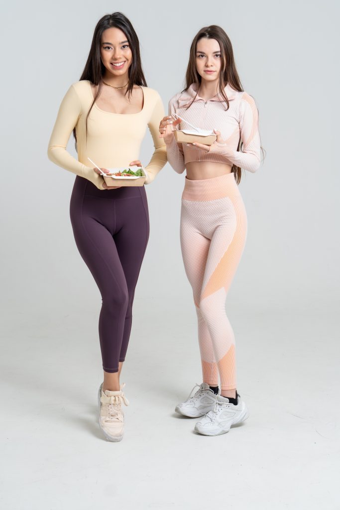 Two individuals in athletic attire holding containers with salad.